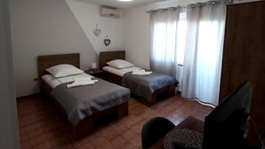 Ein Zimmer mit zwei Betten, einem Schreibtisch, einem Sessel, einem Fernseher und einem Fenster mit Vorhängen.
