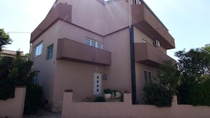 Un edificio de dos plantas con techo plano, entrada central y un pequeño porche con macetas.