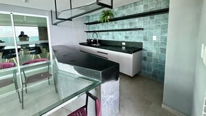 Cocina moderna con una mesa de comedor de vidrio, encimera negra y salpicadero verde azulado.