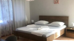 Una cama bien hecha con sábanas blancas, cabecera de madera y una mesita de noche con lámpara.
