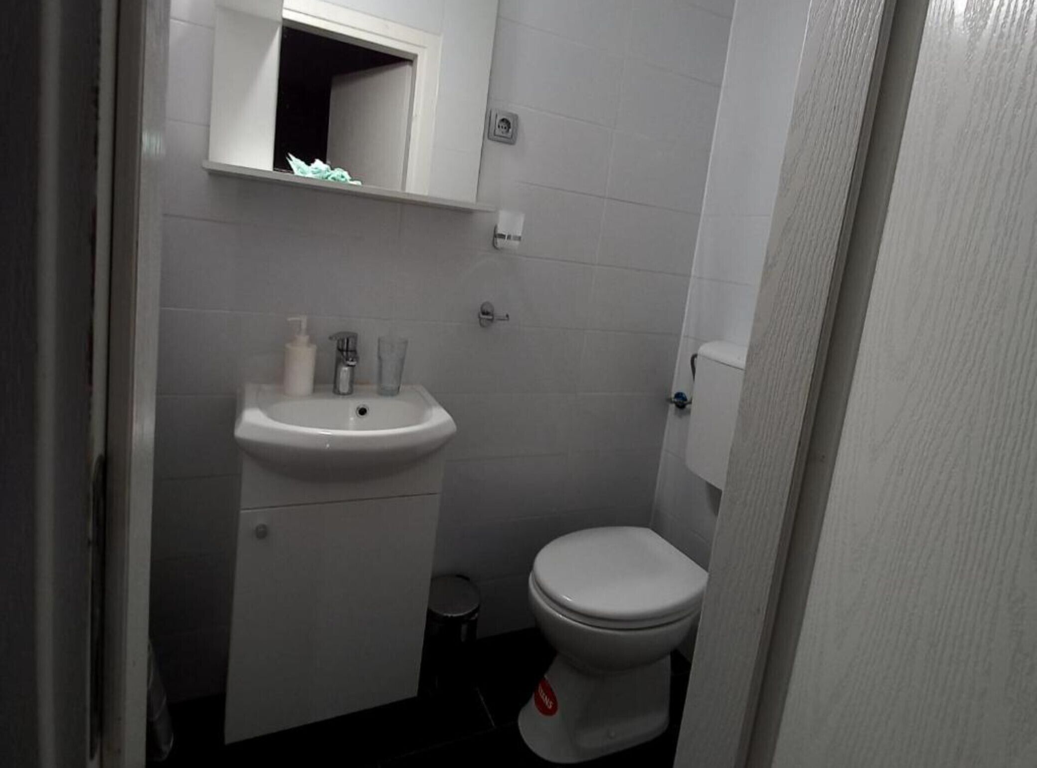 A small, compact bathroom with a white sink, a mirror, and a toilet.