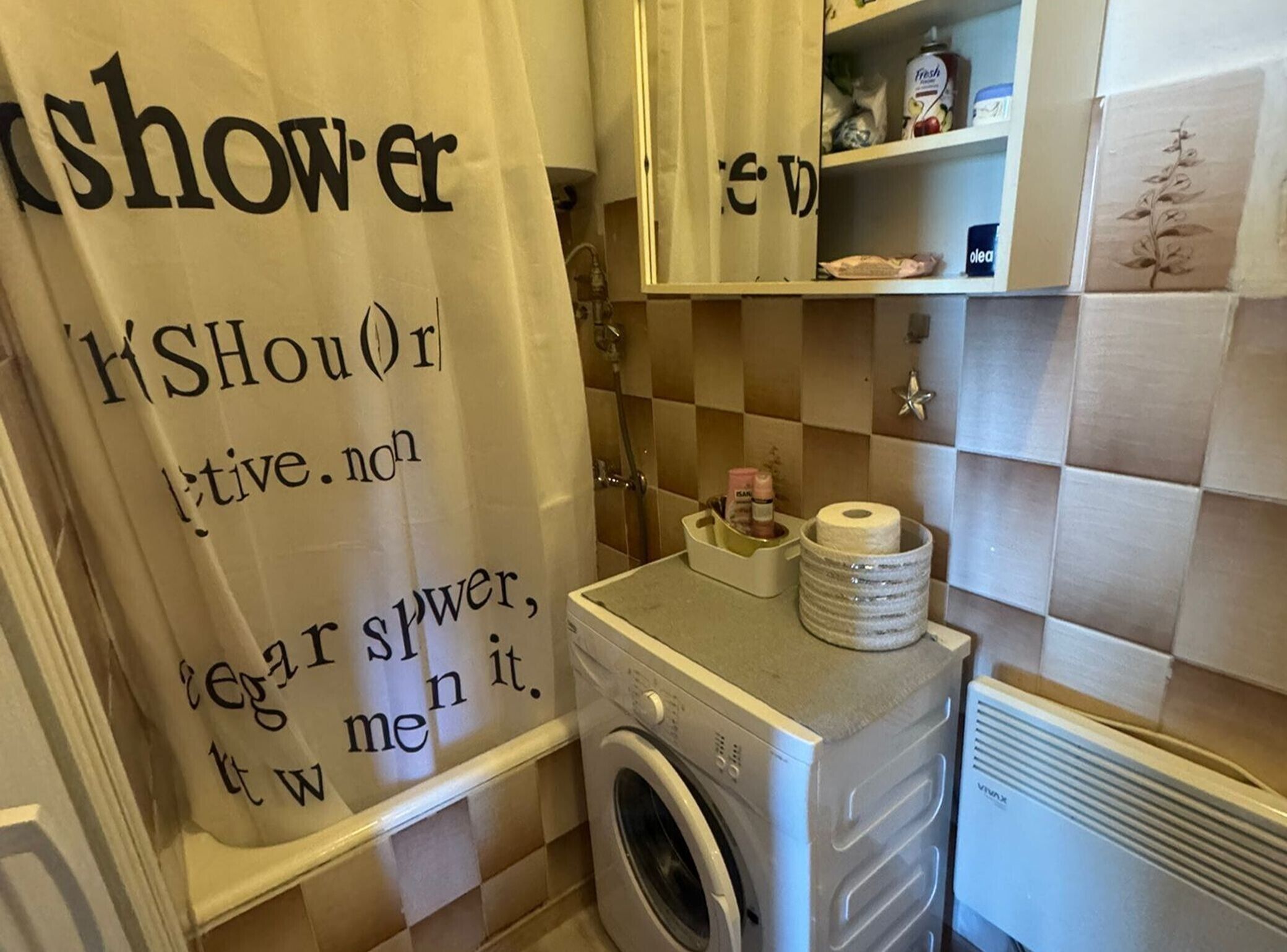 A bathroom with a shower curtain, a washing machine, and a shelf with toiletries.