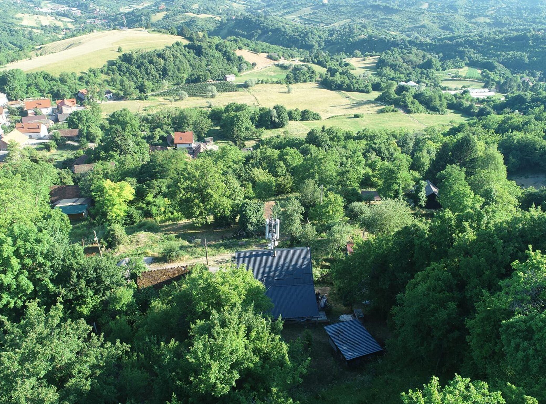 Een luchtbeeld van een landelijk gebied met verspreide huizen, weelderige begroeiing en glooiende heuvels.