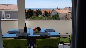 Un balcón con una mesa lista para dos personas, una botella de vino y un frutero.