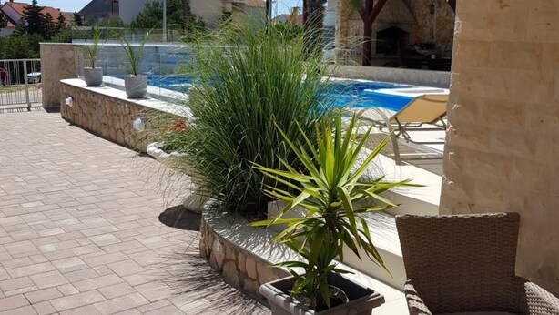 Un espace piscine agrémenté d’un mur en pierre, de plantes en pot et d’un fauteuil en osier.