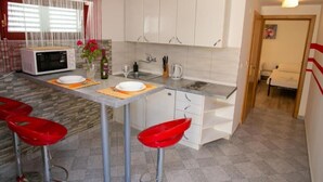 Une cuisine compacte avec des meubles blancs, un four à micro-ondes, un évier et deux tabourets de bar rouges.