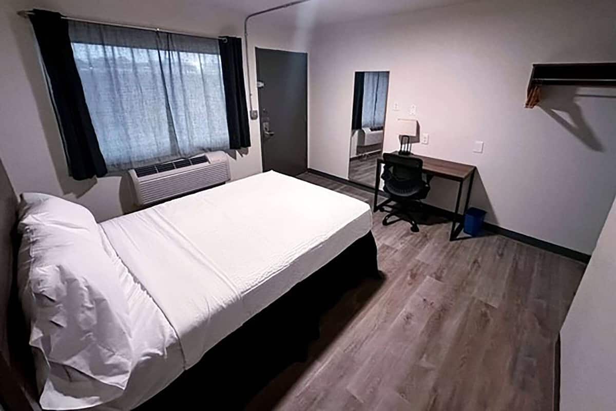 Quarto de hotel com cama, escrivaninha, cadeira e espelho.