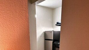 A hotel room with a modern kitchen, a digital thermostat, and a wooden floor. - Studio City Suites, A Travelodge By Wyndham (Texarkana)