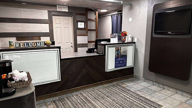 A reception area with a 'WELCOME' sign, a coffee machine, a bulletin board, and a TV mounted on the wall. - Studio City Suites, A Travelodge By Wyndham (Texarkana)