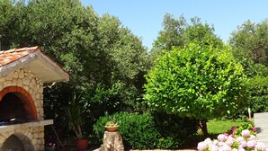 A stone-built outdoor oven, surrounded by lush greenery and flowering plants. - Apartmani Luna - One Bedroom  Apartment (Sukosan)