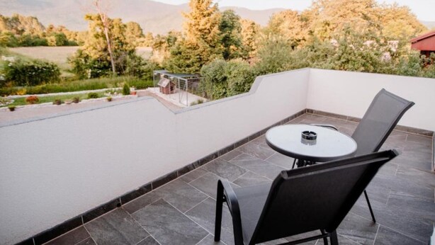 A rooftop terrace with a round table and chairs, surrounded by a white wall and a view of trees and mountains. - Mountain Serenity Rooms - Double Room with Balcony 1 (Korenica)