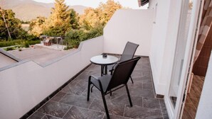Un balcón con mesa y sillas, vistas a árboles y colinas, y un edificio con suelo de baldosas.