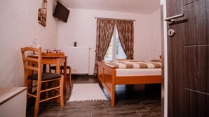 Een knus, compacte kamer met een bed, een bureau en een stoel. Er is een raam met gordijnen, een radiator en een aan de muur bevestigde televisie.