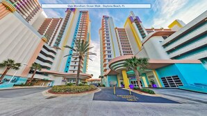 Un hotel modern amb una façana corbada, diversos balcons i una palmera central.