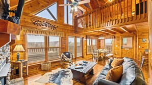 L’intérieur d’une cabane en rondins comprend un coin repas, un canapé, une cheminée et un ventilateur de plafond.