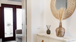 A room with a white dresser, a round mirror, a vase with dried reeds, and a small decorative vase with black sticks.