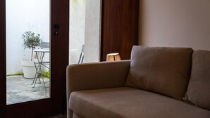 A room with a beige sofa, a small table with a potted plant, and a lamp.