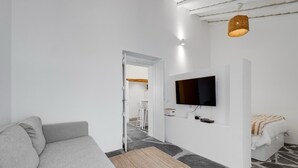 A modern living room with a grey sofa, a flat-screen TV mounted on the wall, and a stone-patterned floor.