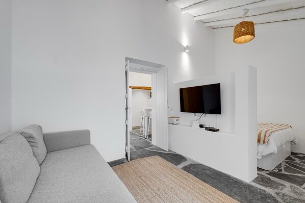 A modern living room with a grey sofa, a flat-screen TV mounted on the wall, and a stone-patterned floor.