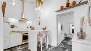 A modern kitchen with white cabinetry, a central island with seating, and a stone floor.