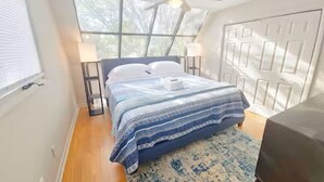 A bedroom with a bed, a ceiling fan, a window, and a door.