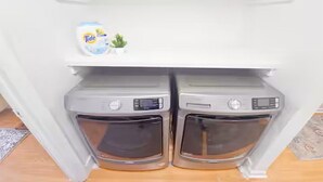 A laundry area with two washing machines and a Tide detergent bottle on a shelf.