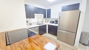 A modern kitchen with dark cabinets, a stainless steel refrigerator, and a wooden countertop.