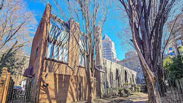 A historic building with a large arched entrance, a brick facade, and a tall tower in the background.