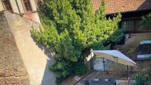Una piscina elevada octogonal con escalera, rodeada por una zona de grava con una mesa y sillas bajo una pérgola.