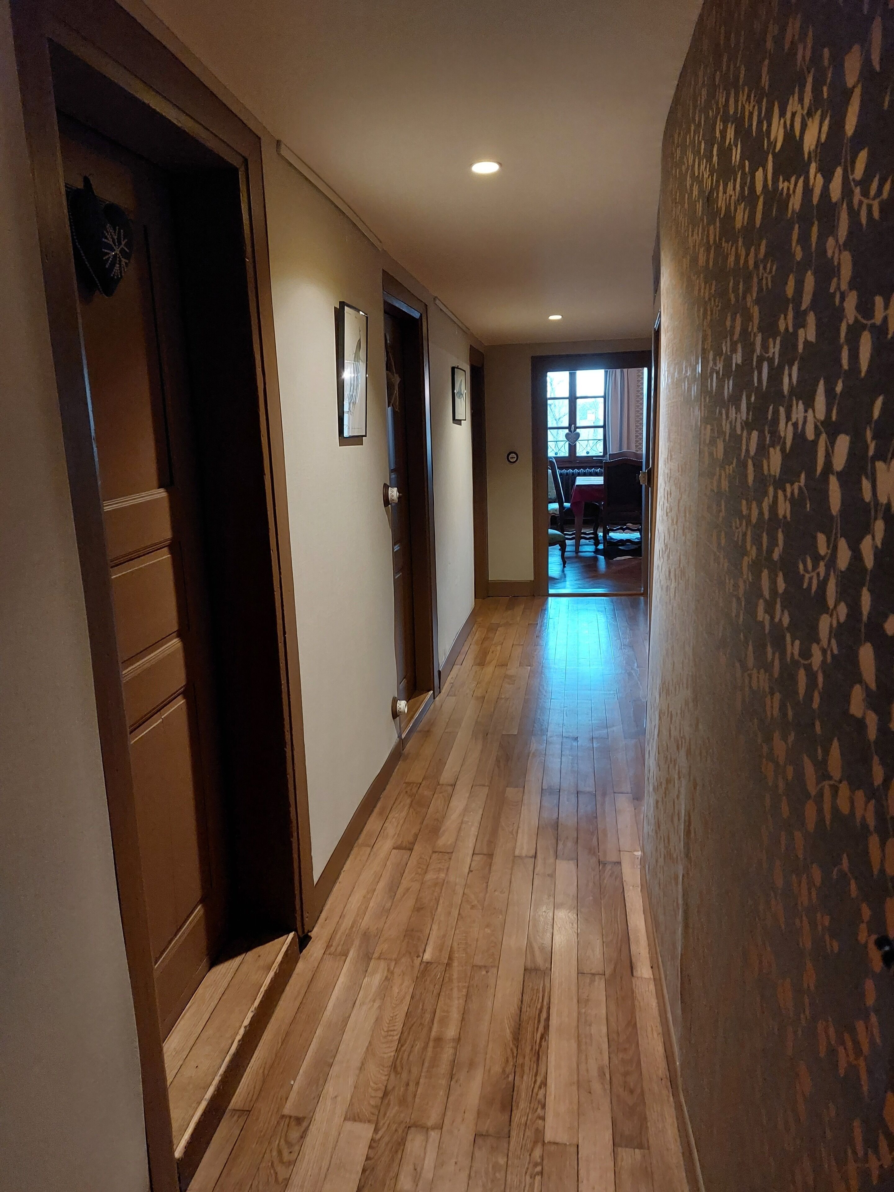 A hallway with wooden flooring, a door on the left, and a patterned wall on the right.