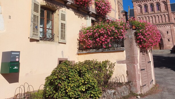 Un edificio tradicional con entramado de madera, jardineras con flores en los alféizares de las ventanas y un muro de piedra al frente.