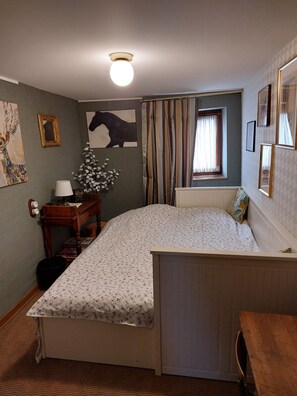 Une chambre à coucher avec un lit, une table de chevet, une lampe, un miroir et une fenêtre avec des rideaux.