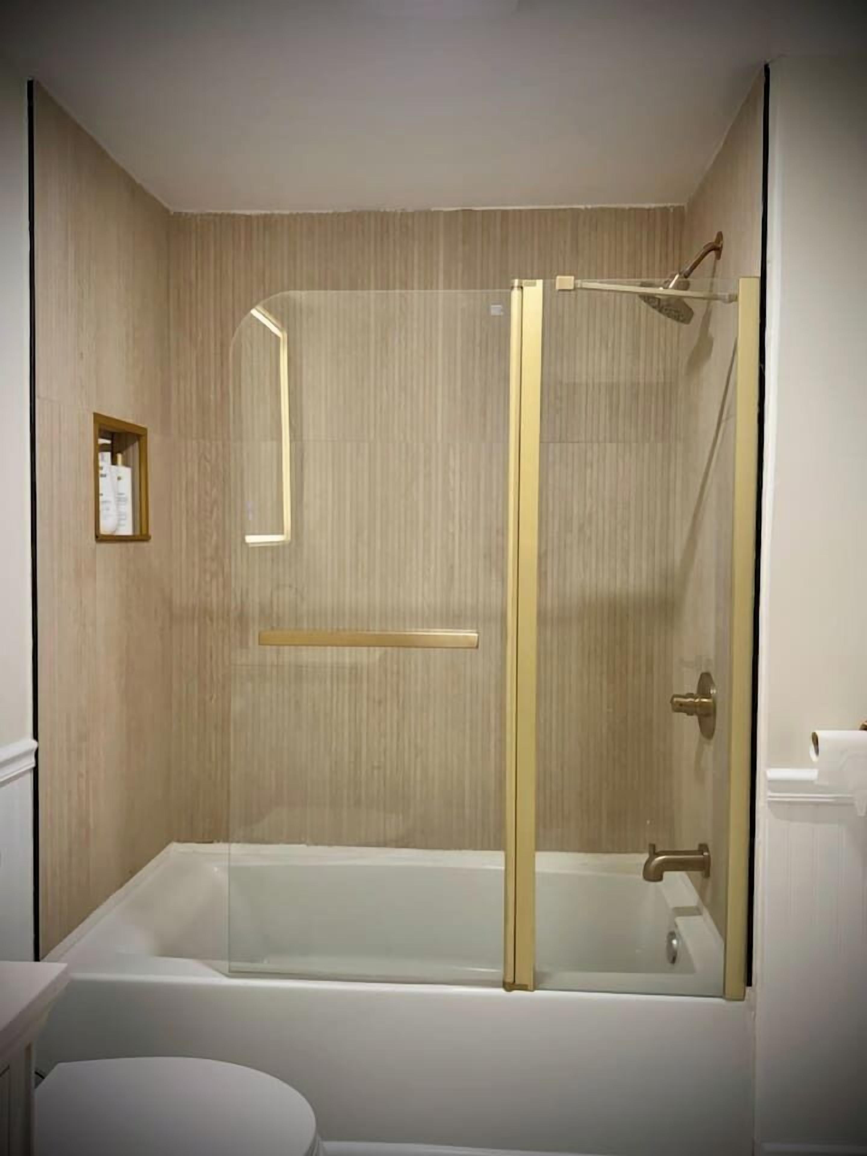 Un baño moderno con ducha envuelta en vidrio, una bañera blanca y un estante pequeño con artículos de tocador.