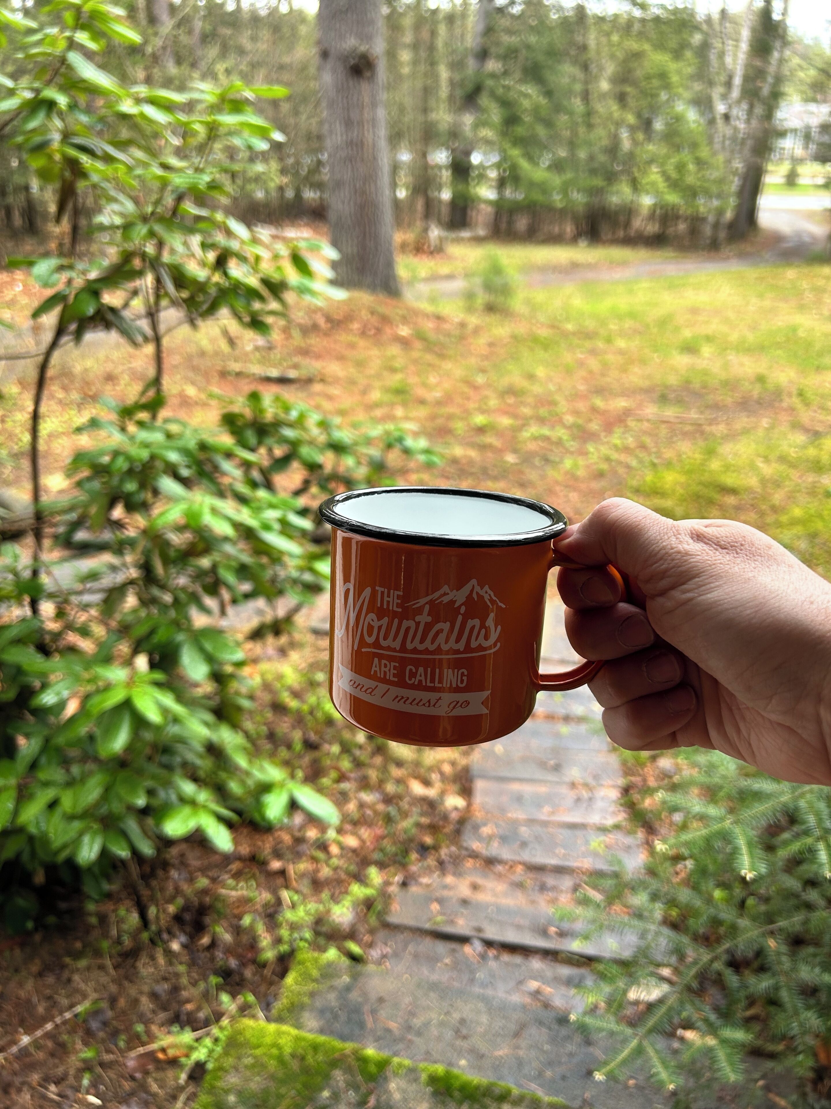 Una mano sosteniendo una taza con un diseño de montaña y texto.