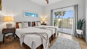 A bedroom with two beds, a ceiling fan, a large window with curtains, a plant, and a view of palm trees. - Hide Tide Hideaway at Carlin Park (Jupiter)