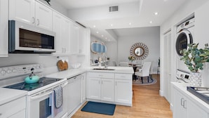 A modern kitchen with white cabinetry, a built-in microwave, and a stove. - Hide Tide Hideaway at Carlin Park (Jupiter)