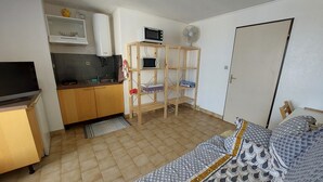 Ein kompakter Wohnraum mit Küchenzeile, einem Bett und einer Holzregaleinheit.