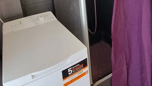 Eine kompakte Wascher- und Trockner-Kombination mit Aufkleber für 5 Jahre Garantie, ein Duschbereich mit lila Vorhang und ein gefliester Boden.