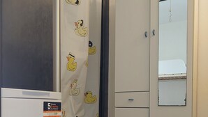Ein kleines Zimmer mit einem weißen Kühlschrank, einem Schrank mit Spiegel und einem Duschvorhang mit Entenmotiven.