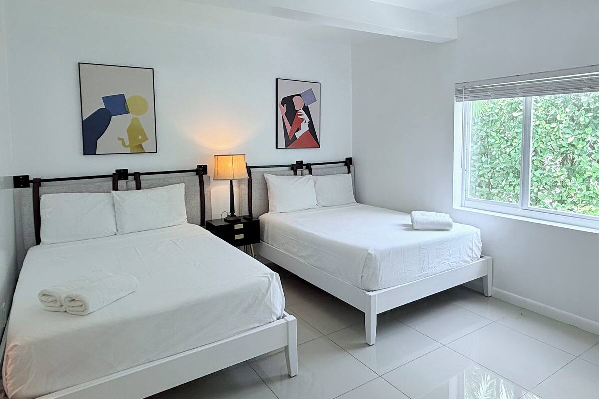 A hotel room with two single beds, a nightstand with a lamp, and artwork on the walls.