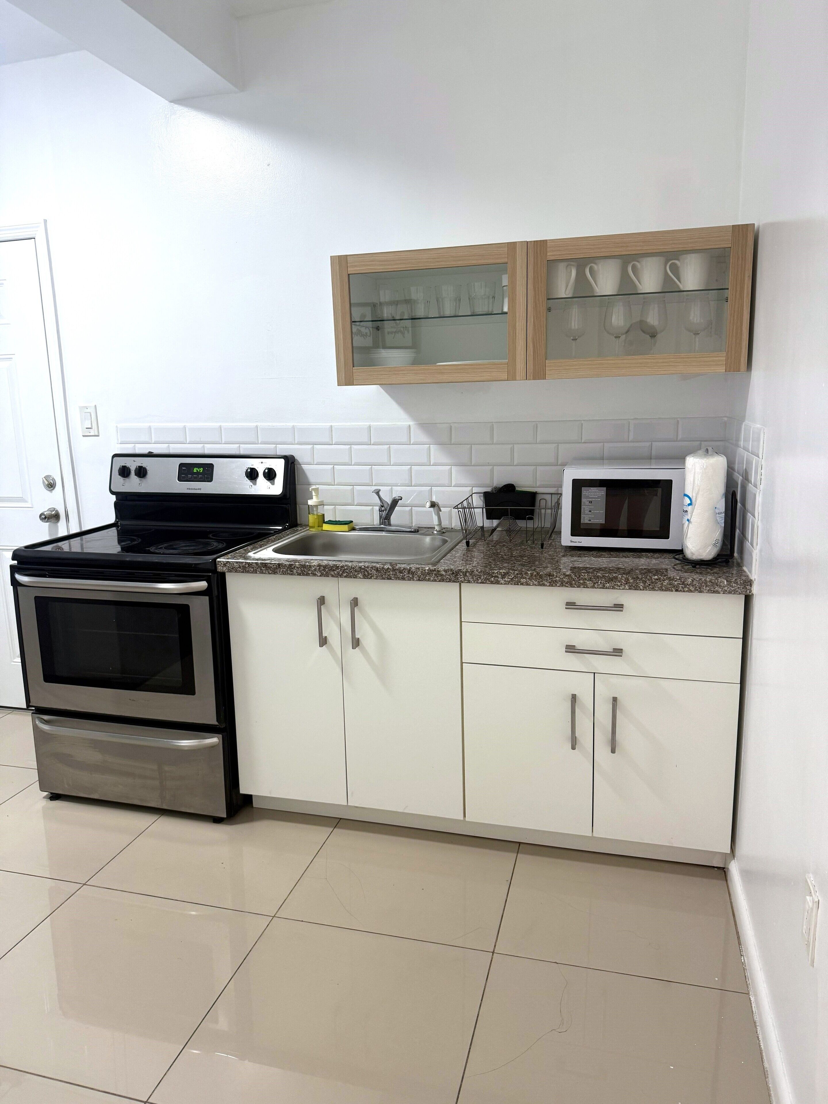 Una cocina con armarios blancos, horno de acero inoxidable, microondas y un mueble con puerta de vidrio sobre el lavamanos.