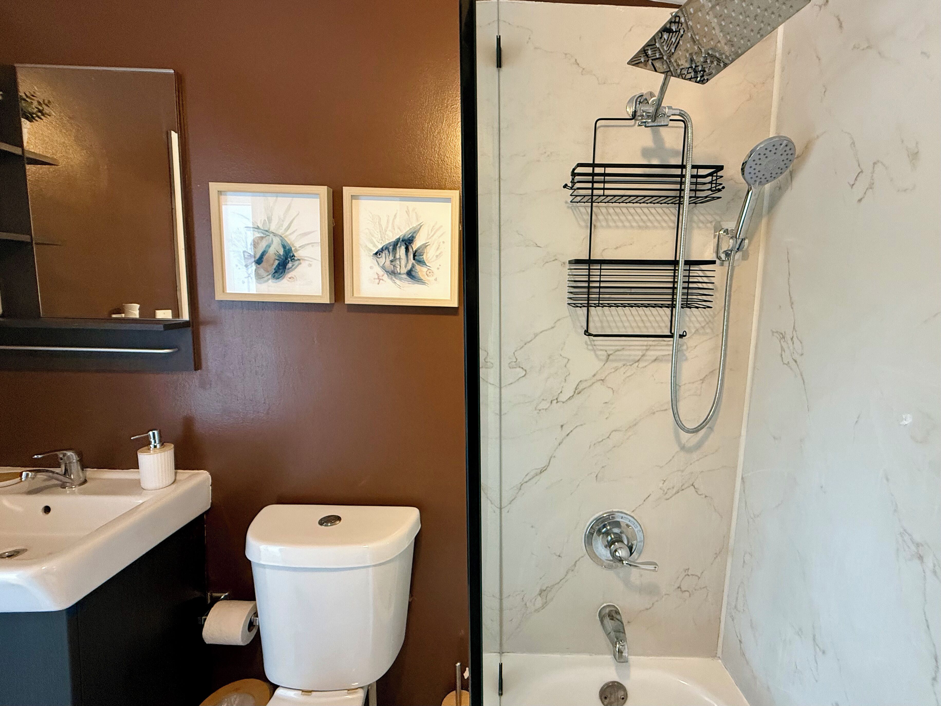 A bathroom with a sink, toilet, and shower. There are two framed pictures on the wall.