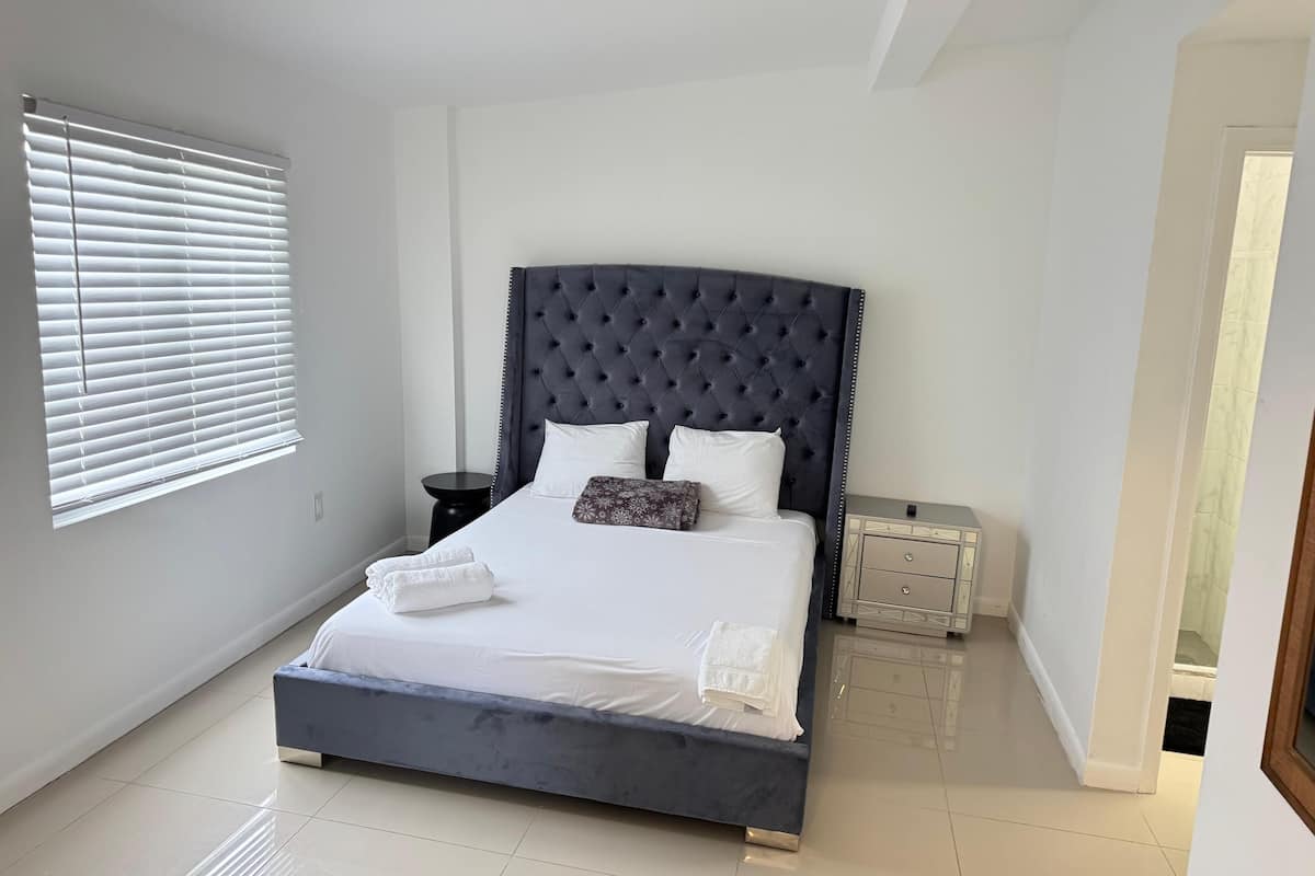 A bedroom with a large bed, a dark headboard, white bedding, and a small bedside table with a lamp.