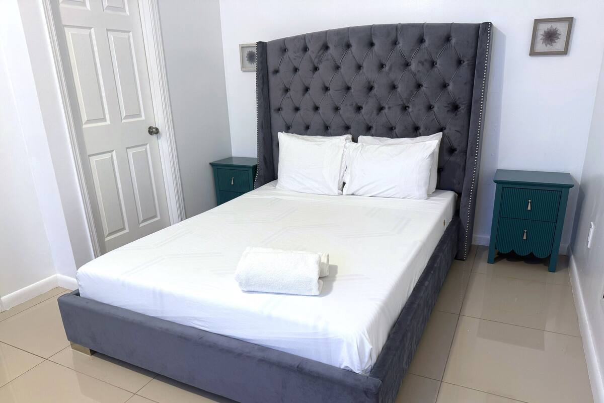 A neatly made bed with white linens and a grey headboard, flanked by teal nightstands with drawers.