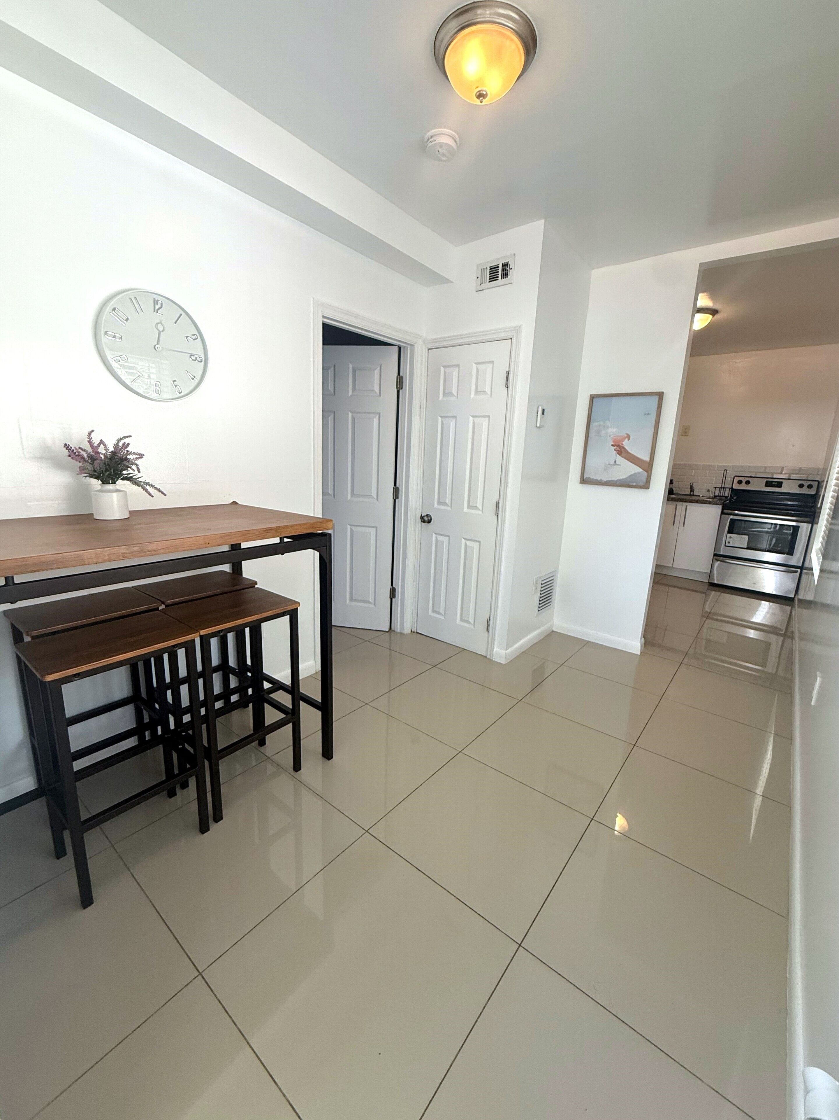 A modern kitchen with a stainless steel oven, a white tiled floor, and a wooden dining table with benches.