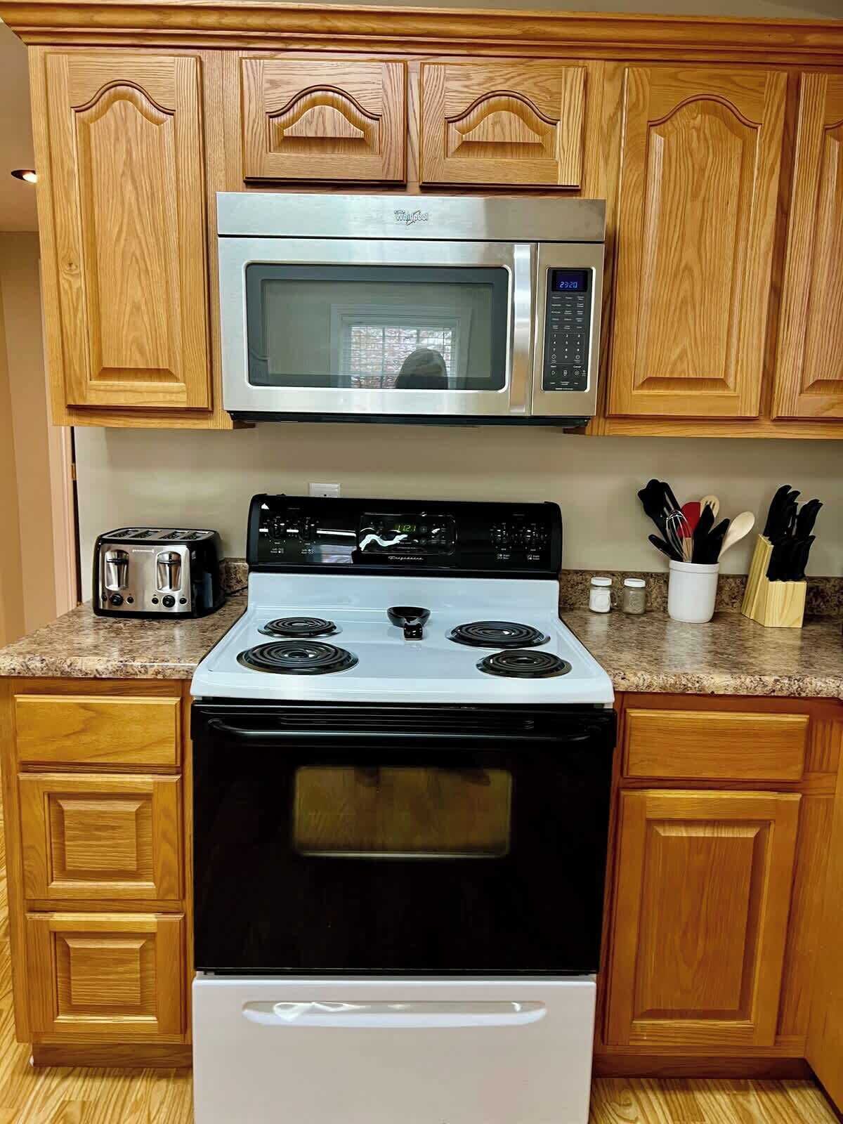 A kitchen with wooden cabinets, a stainless steel microwave, a gas stove, and a toaster.