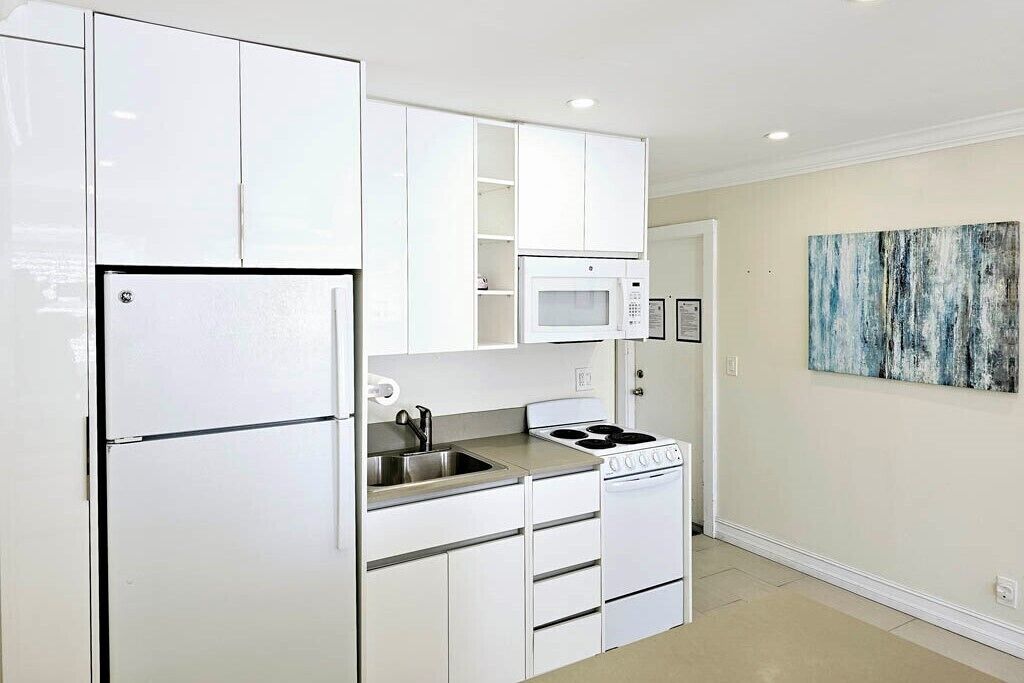 A compact kitchen with white cabinets, a built-in microwave, a stove, and a sink.