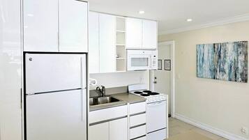 A compact kitchen with white cabinets, a built-in microwave, a stove, and a sink.