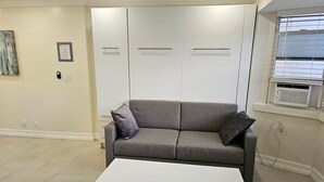 En stue med en grå sofa, et hvidt sofabord og et vindue med rullegardiner.