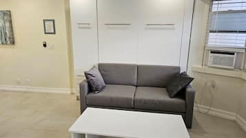A living room with a grey sofa, a white coffee table, and a window with blinds.